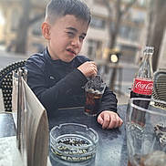 Tyno a rejoint le concours — aidez-le/la à gagner de superbes lots ! child, boy, outdoor, cafe, table, glass, soda, coca_cola, drink, beverage, short_hair, jacket, expression, skeptical, urban, blurred_background, hand, menu, ashtray, seat