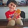 child, boy, smiling, waffle, food, red_shirt, sonic, kitchen, chair, table, plate, backpack, counter, indoor, casual, happy, portrait, snack, furniture, person