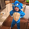 child, costume, blue, sonic_the_hedgehog, smile, barefoot, kitchen, wooden_floor, cabinets, appliance, dishwasher, buddha_statue, countertop, glassware, water_bottle, towel, hooded_onesie, pose, happy, indoors