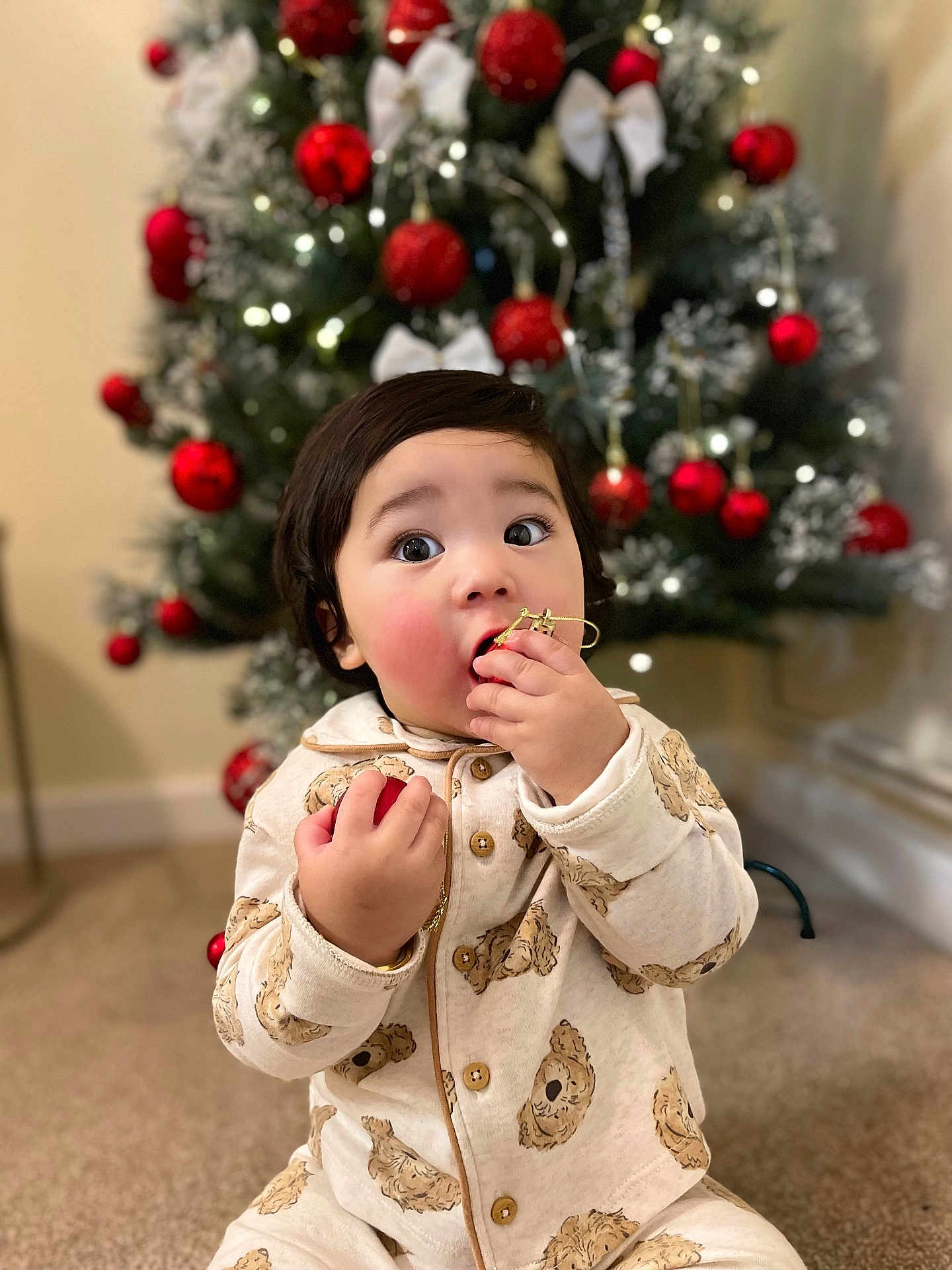 Kesang joined the competition — help win amazing prizes! blurry_background, carpet, child, christmas_tree, cozy, cute, decorations, expression, face, festive, green, holiday, holiday_season, indoor, ornament, pajamas, playful, red, toddler, winter