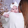 baby, child, woman, headband, white_bow, christmas_tree, holiday, indoor, portrait, soft_lighting, long_hair, holding, warm_clothing, curious_expression, family, celebration, decorations, seasonal, tender_moment, close_up
