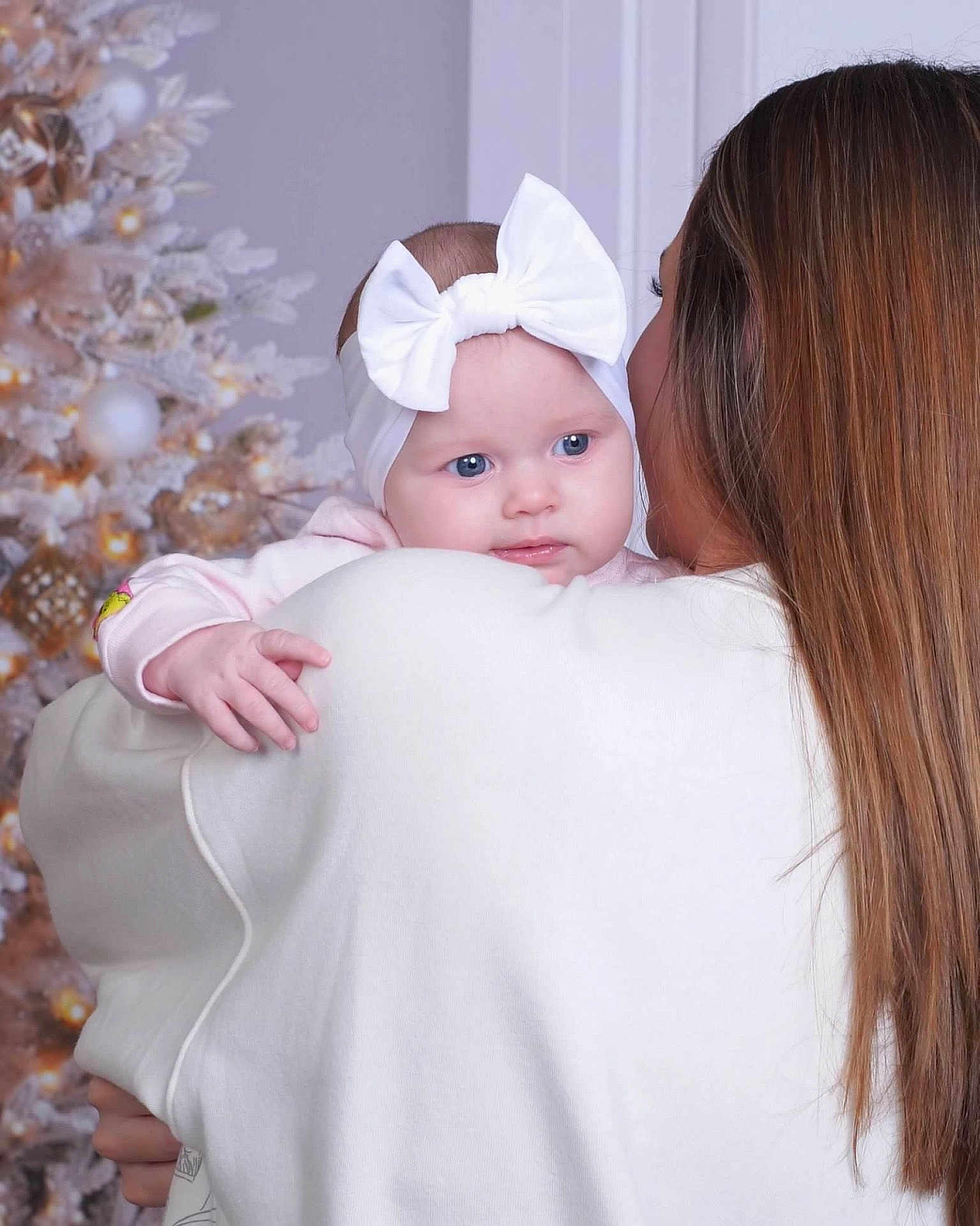 Callie joined the competition — help win amazing prizes! baby, child, woman, headband, white_bow, christmas_tree, holiday, indoor, portrait, soft_lighting, long_hair, holding, warm_clothing, curious_expression, family, celebration, decorations, seasonal, tender_moment, close_up