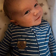 Jude is registered to the contest to win money with this photo: baby, infant, smile, face, blue_onesie, striped_clothing, bear_patch, lying_down, closeup, child, cute, cozy, soft_background, stars_pattern, young_child, portrait, happy, person, sleepwear, indoors