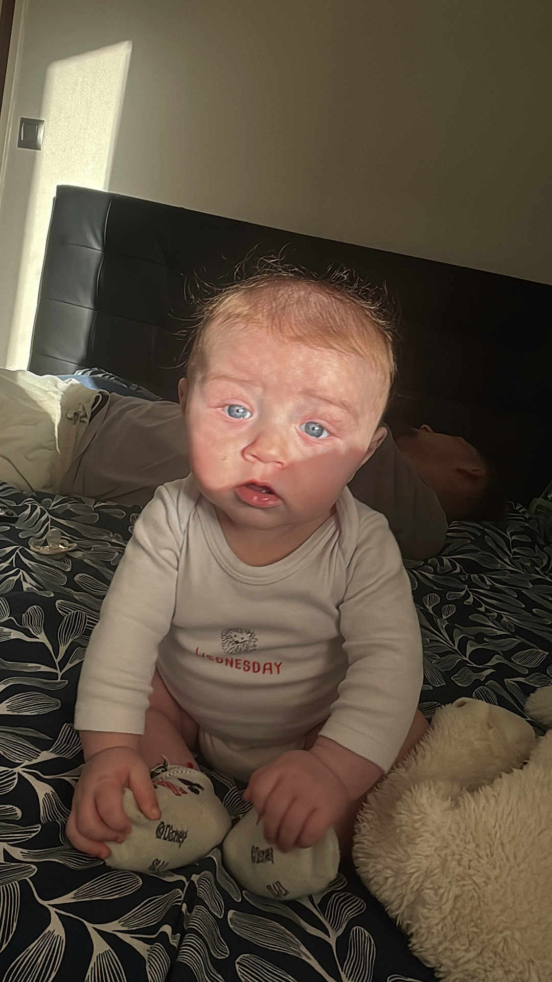 Elio Briche participe au concours pour gagner de l'argent avec cette photo : baby, infant, child, bed, bedding, headboard, pacifier, onesie, sitting, blue_eyes, sunlight, shadow, adult_in_background, plush_toy, socks, hands, blanket, pattern, indoor, portrait