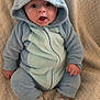 Elio Briche participe au concours pour gagner de l'argent avec cette photo : baby, infant, hooded_onesie, blue_onesie, plush_costume, sitting, blanket, cute, surprised_expression, open_mouth, big_eyes, face, hands, socks, soft_texture, cozy, portrait, indoor, quilt, closeup
