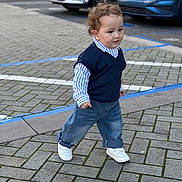 Yanis is registered to the contest to win money with this photo: toddler, child, walking, street, pavement, jeans, shirt, vest, sneakers, cars, parking_lot, outdoor, curb, sidewalk, person, fashion, casual, young_child, daytime, urban