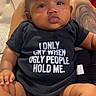 baby, child, onesie, sitting, tattoo, indoor, furniture, person, clothing, expression, cute, skin, hand, footwear, sock, humor, text_on_clothing, black_clothing, infant, portrait