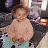 air_conditioner, bed, blanket, child, clothing, curly_hair, curtain, face, fan, furniture, happy, heater, indoor, jacket, pants, person, room, smiling, toddler, window