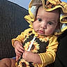 baby, child, infant, sunflower, hat, bonnet, yellow_clothing, onesie, couch, fabric, indoor, person, portrait, cute, face, expression, hand, sitting, skin, eyes