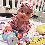 Andi is registered to the contest to win money with this photo: baby, infant, pink_headband, playmat, toy_bottle, crib, nursery, flower_decoration, tummy_time, curious, child, indoors, cute, clothing, hand, face, expression, soft_lighting, smile, person