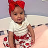 baby, child, infant, red_bow, headband, ladybug_pants, white_shirt, pink_bed, crib, purple_wall, smiling, sitting, cute, indoors, person, young_child, portrait, happy, baby_girl, clothing