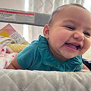 Andi is registered to the contest to win money with this photo: baby, child, smile, laugh, teal_clothing, playpen, blanket, quilt, indoor, happy, face, infant, cute, portrait, person, skin, head, cheerful, fun, young