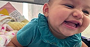 Andi is registered to the contest to win money with this photo: baby, blanket, cheerful, child, cute, face, fun, happy, head, indoor, infant, laugh, person, playpen, portrait, quilt, skin, smile, teal_clothing, young