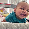baby, child, smile, laugh, teal_clothing, playpen, blanket, quilt, indoor, happy, face, infant, cute, portrait, person, skin, head, cheerful, fun, young