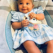 Malia is registered to the contest to win money with this photo: baby, child, smiling, blue_dress, headband, toy, soft_toy, sitting, indoor, patterned_seat, cute, happy, infant, clothing, closeup, portrait, baby_girl, skin, hands, feet