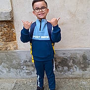 Mio a rejoint le concours — aidez-le/la à gagner de superbes lots ! backpack, boy, casual_clothing, child, concrete, footwear, glasses, happy, outdoor, person, pose, short_hair, smile, sport_outfit, standing, street, thumbs_up, urban, wall, young