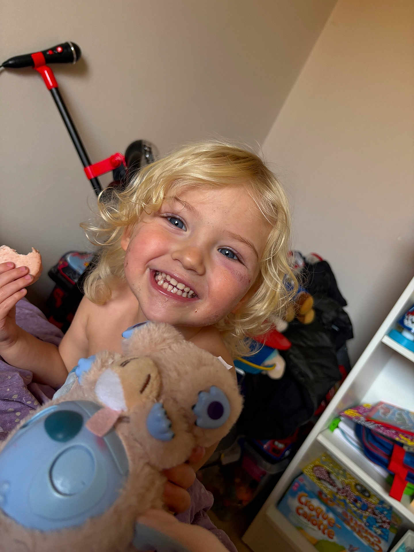 Maddy a rejoint le concours — aidez-le/la à gagner de superbes lots ! child, smile, blonde_hair, blue_eyes, plush_toy, indoor, toy, bookshelf, book, clutter, happy, person, face, playful, messy_room, curly_hair, holding, cute, portrait, casual
