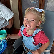 Maddy a rejoint le concours — aidez-le/la à gagner de superbes lots ! toddler, child, smiling, laughing, blonde_hair, pigtails, hair_bow, denim_overalls, red_shirt, high_chair, cup, indoor, window, curtains, wooden_door, glass_table, adult_partial, happy, person, seated