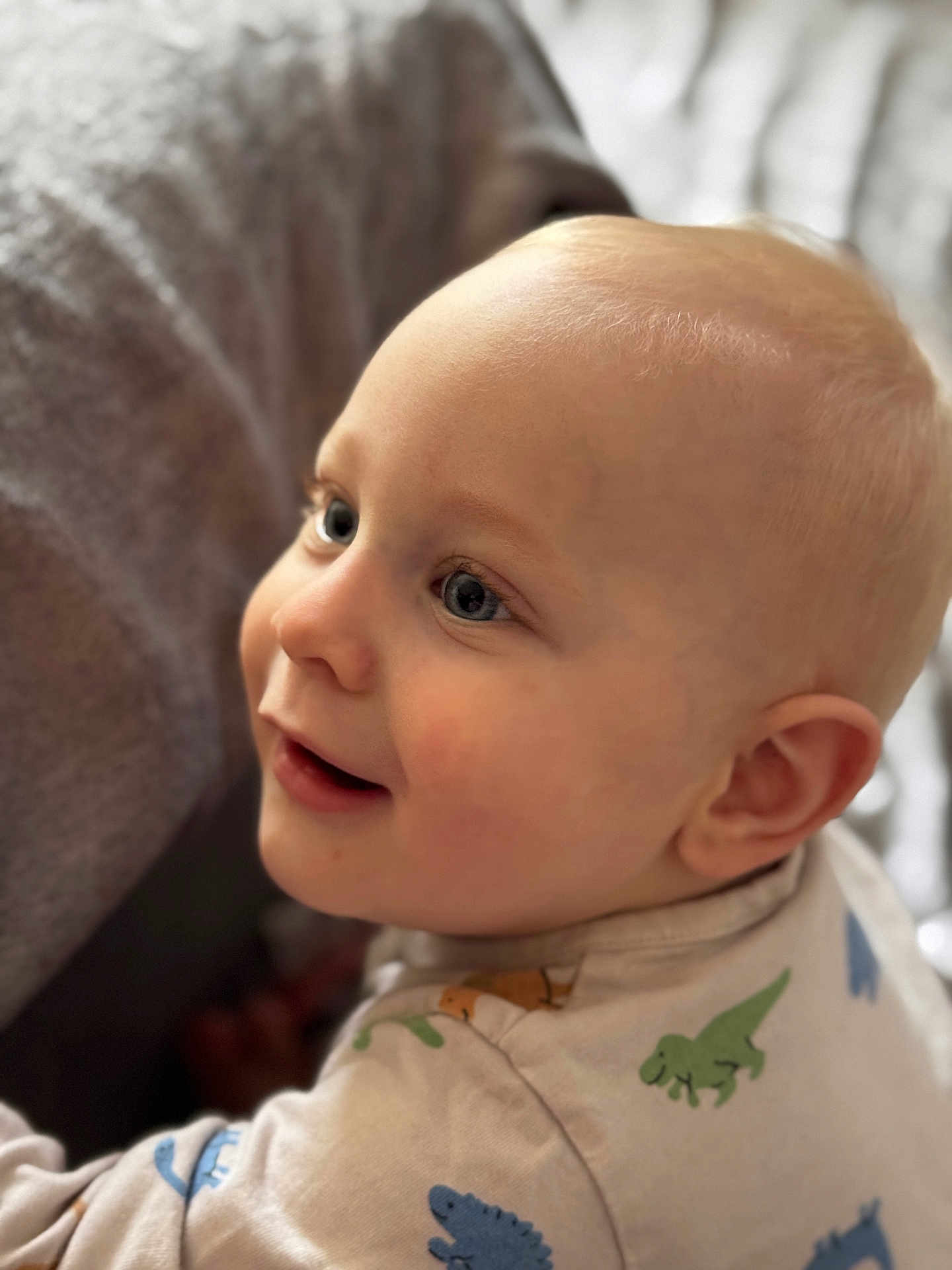 Emmett a rejoint le concours — aidez-le/la à gagner de superbes lots ! baby, blond_hair, blue_eyes, cheek, child, closeup, curious, cute, dinosaur_print, ear, face, happy, indoors, infant, onesie, person, portrait, skin, smile, soft_light