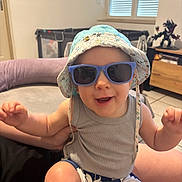Emmett participe au concours pour gagner de l'argent avec cette photo : action_figure, baby, child, floor_tiles, furniture, hand, hat, indoor, joyful, living_room, person, playful, portrait, shorts, skin, smiling, sunglasses, tank_top, toddler, window