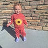 toddler, child, smiling, standing, outdoor, sunlight, sunflower, sweatshirt, tracksuit, red_clothing, purple_shoes, clogs, brick_wall, stone_wall, patio, shadow, portrait, full_body, happy, fashion