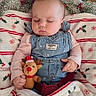 baby, sleeping, christmas, holiday, reindeer_toy, plush_toy, denim_overalls, pink_shirt, blanket, christmas_tree, ornaments, garland, red, green, festive, infant, portrait, indoors, cozy, peaceful