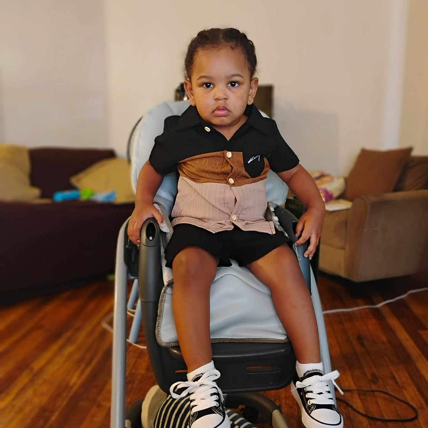 Xaiver is registered to the contest to win money with this photo: toddler, child, high_chair, sneakers, socks, shirt, shorts, living_room, sofa, cushions, wooden_floor, plush_toy, furniture, indoor, person, portrait, floor, footwear, casual_clothing, seated