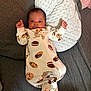 baby, infant, onesie, cookie_pattern, pillow, couch, sofa, fabric, face, person, sleepwear, baby_clothing, indoors, cute, newborn, resting, raised_hands, texture, soft, comfort
