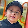 child, boy, face, smile, cap, hoodie, outdoor, playground, portrait, young, happy, casual_clothing, daylight, headwear, person, childhood, expression, greenery, blurred_background, cute