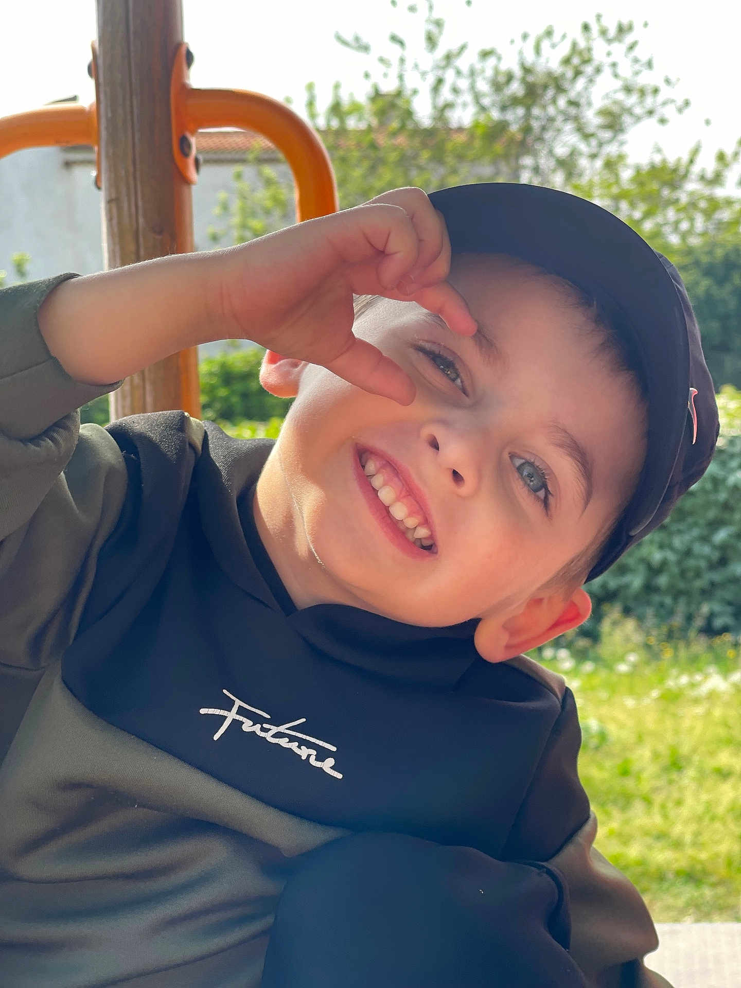 Tyago participe au concours pour gagner de l'argent avec cette photo : child, boy, smile, cap, hoodie, hand_gesture, outdoor, playground, sunlight, greenery, face, happy, casual_clothing, portrait, young, nature, daylight, person, expression, leisure