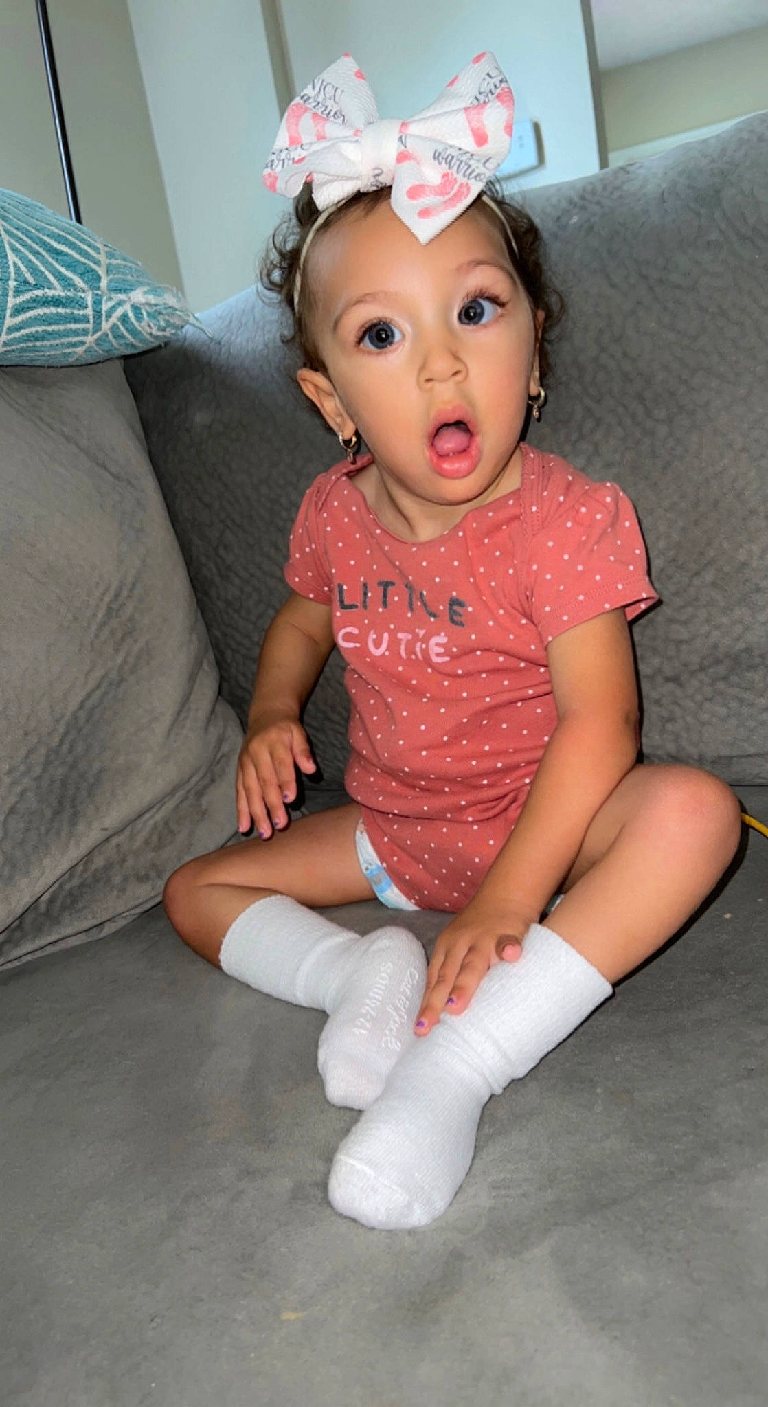 Arya is registered to the contest to win money with this photo: arm, baby_toddler_clothing, child, costume_hat, embellishment, face, finger, fun, happy, head, human_leg, knee, leg, neck, person, pink, sleeve, sock, surprise, t_shirt