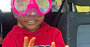 Willie is registered to the contest to win money with this photo: back_seat, bright_colors, car_interior, casual_clothing, child, fun, goggles, hair_up, happy, indoors, peace_sign, person, playful, portrait, red_hoodie, seatbelt, smiling, transportation, window, young