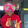 back_seat, bright_colors, car_interior, casual_clothing, child, fun, goggles, hair_up, happy, indoors, peace_sign, person, playful, portrait, red_hoodie, seatbelt, smiling, transportation, window, young