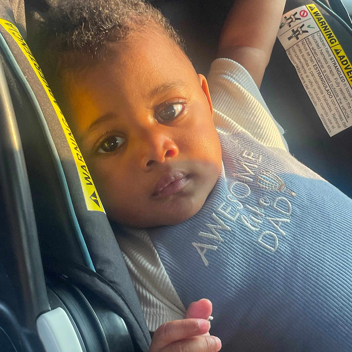 Uriyah Barfield is registered to the contest to win money with this photo: baby, car_seat, child, close_up, clothing, curly_hair, cute, expression, face, hand, indoor, infant, person, portrait, seat, seatbelt, sunlight, text_on_clothing, toddler, warning_label