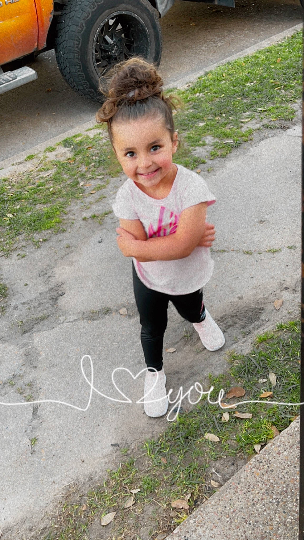 Paisleigh is registered to the contest to win money with this photo: asphalt, automotive_tire, face, grass, happy, joy, leg, leisure, morning, people_in_nature, person, plant, road_surface, sidewalk, sleeve, smile, standing, t_shirt, tire, toddler