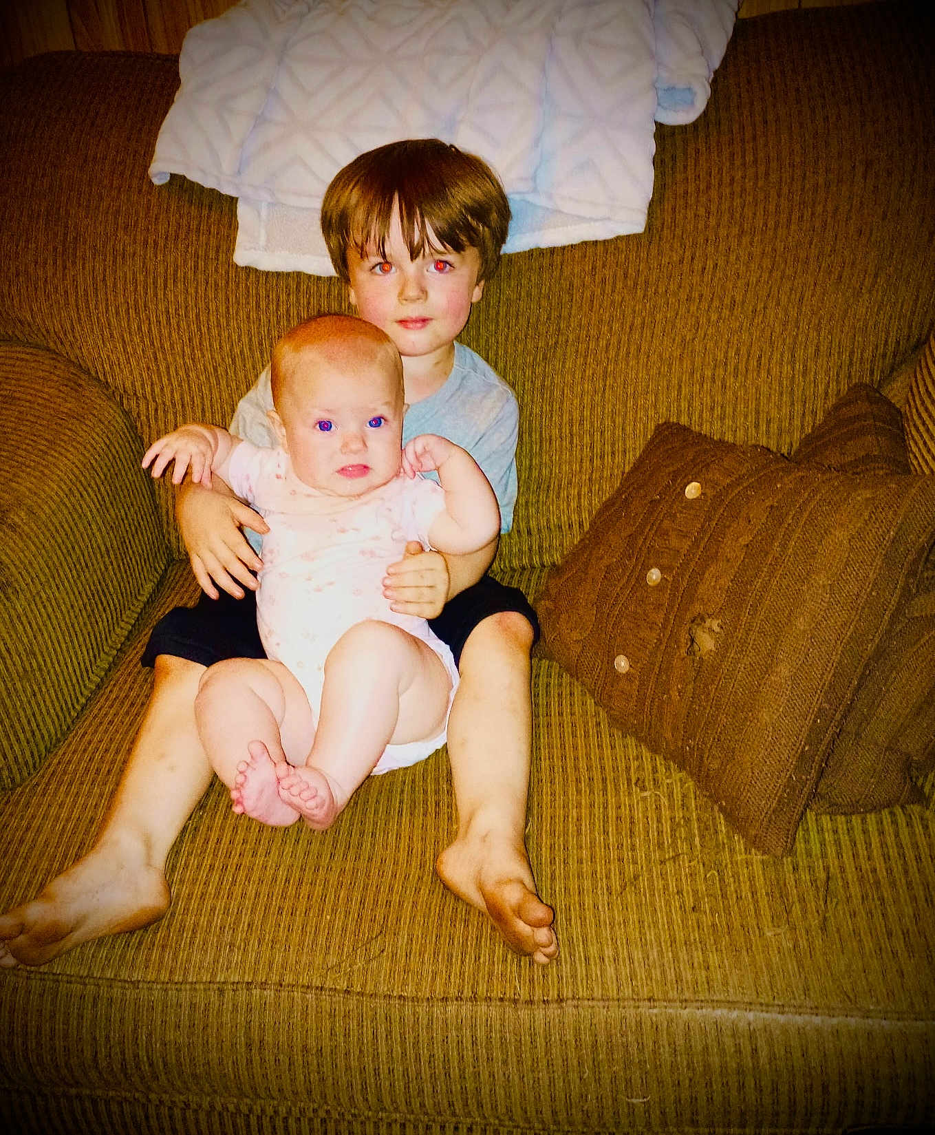 Haislynn joined the competition — help win amazing prizes! baby, child, couch, pillow, blanket, sitting, indoors, barefoot, red_eye, face, person, young_child, holding, furniture, home, cozy, casual, portrait, clothing, brown