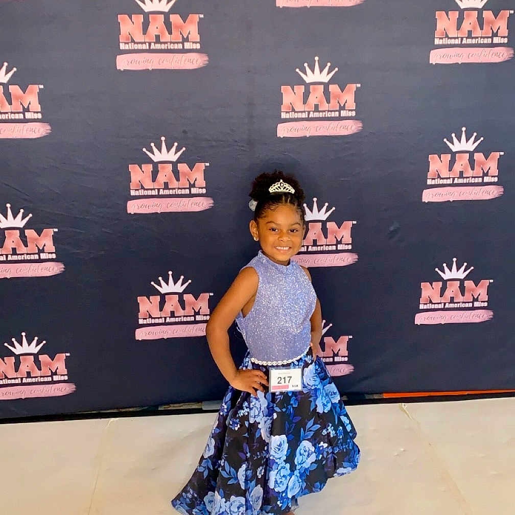 Miata is registered to the contest to win money with this photo: blackboard, blackhair, child, clothing, dress, fashion, female, footwear, formalwear, girl, hair, performer, person, premiere, sandal, shoe, skirt, sleeve, soloperformance, standing