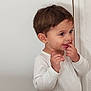brown_pants, casual_clothing, child, curious, cute, door, expression, happy, human, indoors, person, playful, portrait, short_hair, small_child, smiling, standing, toddler, white_shirt, young_child