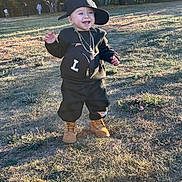 Luis joined the competition — help win amazing prizes! toddler, child, boy, outdoor, grass, sunlight, trees, hat, cap, black_clothing, boots, smile, happy, necklace, backpack, standing, daylight, fashion, casual, park