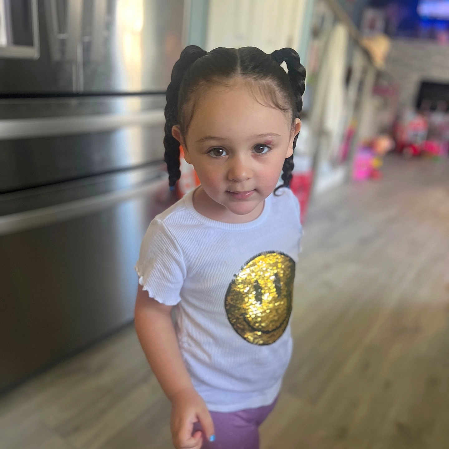 Emilia is registered to the contest to win money with this photo: appliance, braids, casual_clothing, child, curious, flooring, girl, gold_sequin, home, indoor, kitchen, person, pigtails, portrait, purple_pants, refrigerator, smiley_face, standing, white_shirt, young_child
