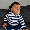 Wilson a rejoint le concours — aidez-le/la à gagner de superbes lots ! baby, child, pacifier, striped_shirt, navy_pants, white_socks, couch, gray_couch, indoor, curious, sitting, young_child, portrait, casual_clothing, cute, infant, home, furniture, person, looking_away