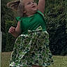Bonnie-Leigh joined the competition — help win amazing prizes! child, toddler, girl, outdoor, garden, grass, hedge, dress, green_clothing, shamrock, clover, patterned_dress, pink_watch, white_socks, standing, reaching, playful, portrait, daylight, smiling
