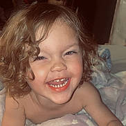 Gunnar joined the competition — help win amazing prizes! child, toddler, curly_hair, smile, laughing, teeth, blanket, bed, indoor, portrait, closeup, happy, cozy, bare_shoulders, skin, candid, bedroom, clothing_hanging, playful, infant