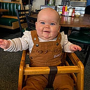 Charlee is registered to the contest to win money with this photo: baby, child, smiling, highchair, restaurant, diner, blue_eyes, overalls, brown_overall, wooden_bar, table, condiments, ketchup, mustard, chair, booth_seating, indoor, cute, plush_shoes, portrait