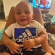 Kiair is registered to the contest to win money with this photo: adidas, baby, bed, blanket, child, cozy, furniture, hair, hands, happy, indoor, legs, living_room, person, relaxing, shorts, sleeping_child, smiling, television, tshirt