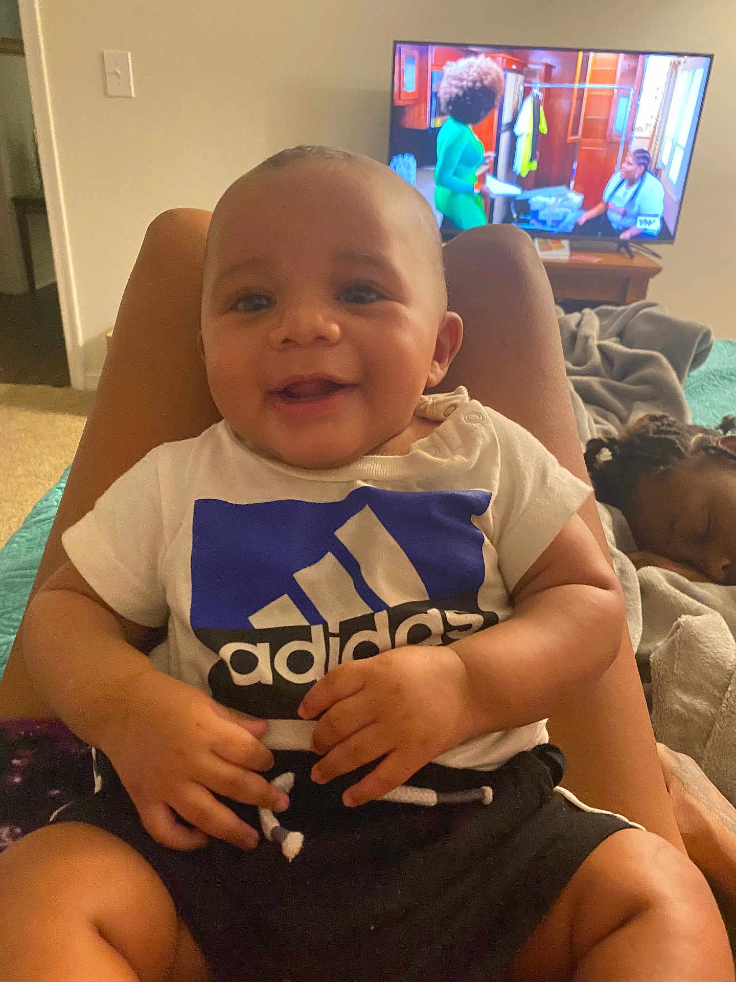 Kiair is registered to the contest to win money with this photo: adidas, baby, bed, blanket, child, cozy, furniture, hair, hands, happy, indoor, legs, living_room, person, relaxing, shorts, sleeping_child, smiling, television, tshirt