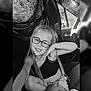 black_and_white, braids, car_interior, casual_clothing, child, cute, fabric, girl, glasses, hand_on_chin, happy, playful, portrait, seat, seat_cover, sitting, smiling, steering_wheel, window, young