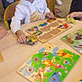 boy, child, colorful, furniture, game, happy, hoodie, indoor, learning, legs, people, playing, puzzle, seated, shoes, smiling, table, tattoo, watch, wooden_toy