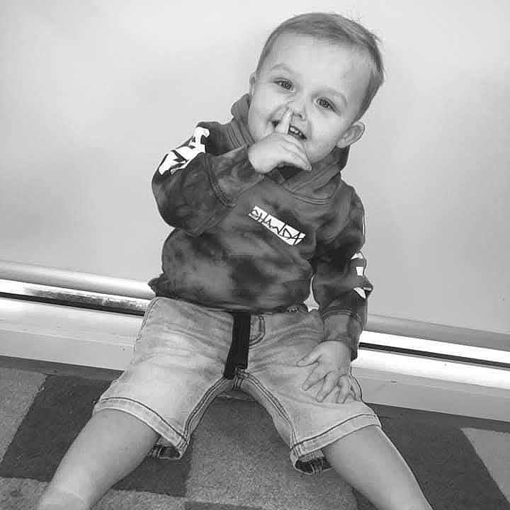 Daxton is registered to the contest to win money with this photo: background, barefoot, carpet, casual_clothing, cheeky, child, floor, gesture, happy, hoodie, indoor, monochrome, person, playful, portrait, shorts, sitting, smiling, toddler, young_child