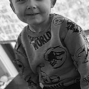 Daxton is registered to the contest to win money with this photo: background, black_and_white, casual, child, clothing, cute, dinosaur, face, happy, home, indoor, light, person, playful, portrait, sitting, smiling, sweatshirt, table, young